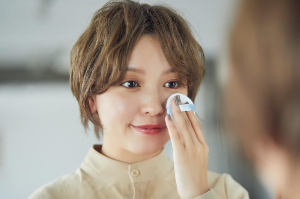 顔にパフでファンデーションを塗る女性の画像