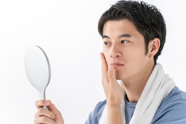 手鏡を見ながら肌をチェックしている男性